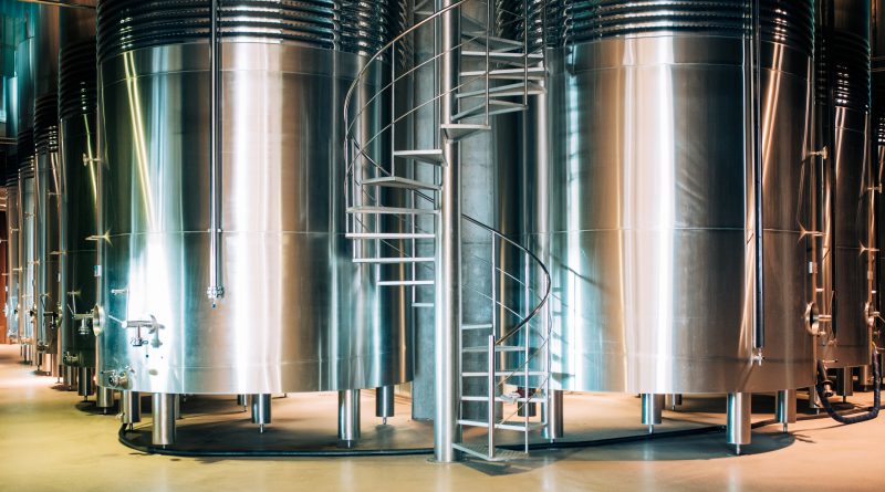 Przemysłowy zbiornik na wodę stalowy o dużej pojemności w nowoczesnym zakładzie. Widoczne kręcone schody stalowe prowadzące na szczyt zbiornika.