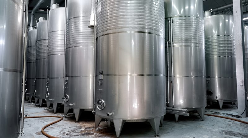 Rząd przemysłowych zbiorników na wodę stalowych w hali produkcyjnej. Zbiorniki wykonane ze stali nierdzewnej, widoczne orurowanie i włazy inspekcyjne.